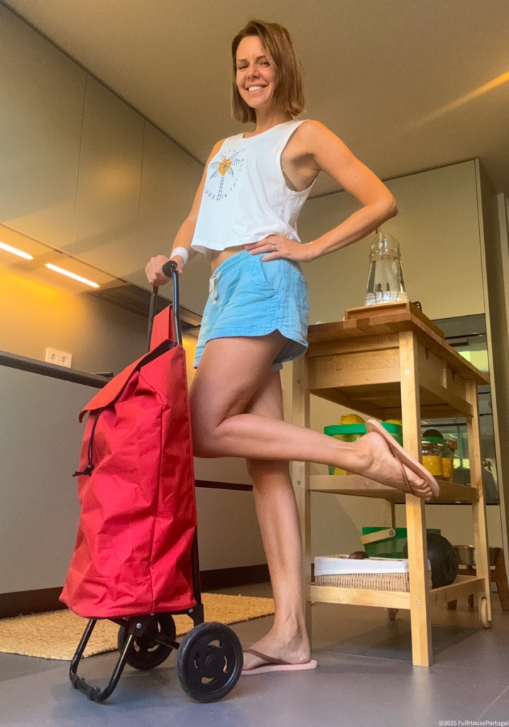 Woman smiling with red shopping trolley in Portuguese kitchen, ready for a market trip in Portugal.